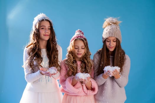 Three beautiful fashionable girl girlfriends in a winter snow cap blue background