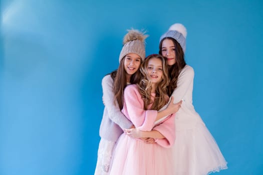 Three beautiful fashionable girl girlfriends in a winter snow cap blue background