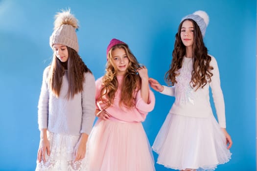 Three beautiful fashionable girl girlfriends in a winter snow cap blue background