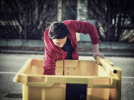Young poor man searching inside garbage bin for stuff still usable or useful