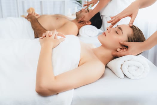 Caucasian couple enjoying relaxing anti-stress head massage and pampering facial beauty skin recreation leisure in dayspa modern light ambient at luxury resort or hotel spa salon. Quiescent