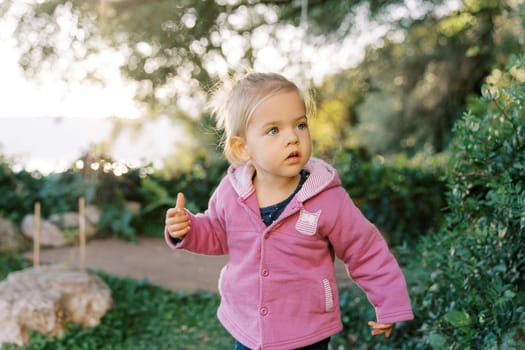 Little girl stands half-turned in the park with her mouth open in surprise. High quality photo