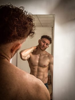 A shirtless man looking at himself in the mirror