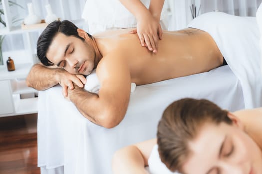 Caucasian couple customer enjoying relaxing anti-stress spa massage and pampering with beauty skin recreation leisure in day light ambient salon spa at luxury resort or hotel. Quiescent