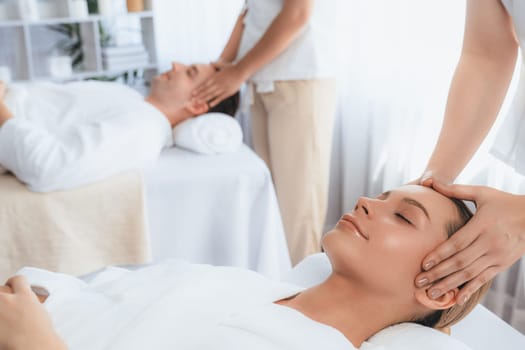 Caucasian couple enjoying relaxing anti-stress head massage and pampering facial beauty skin recreation leisure in dayspa modern light ambient at luxury resort or hotel spa salon. Quiescent