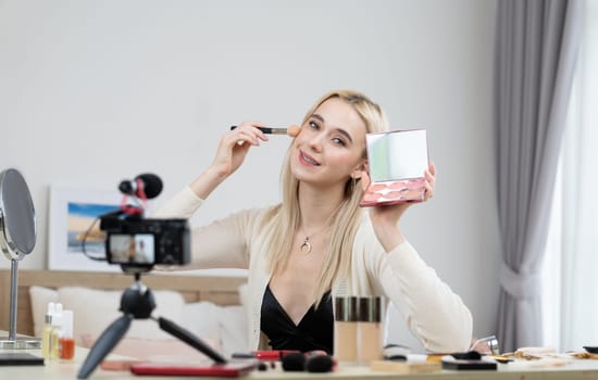 Young woman making beauty and cosmetic tutorial video content for social media. Beauty blogger smiles to camera while showing how to beauty care to audience or followers. Blithe