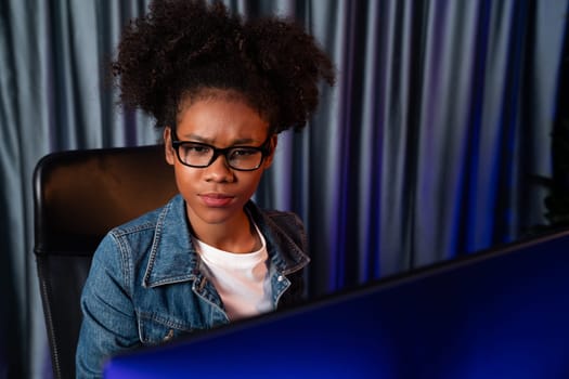 Young African American creator woman with serious face, thinking carefully and looking at final project document on laptop for planing next sequence. Concept of work at neat home place. Tastemaker.
