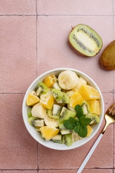 Bowl of healthy fresh fruit salad on ceramic background. Top view.