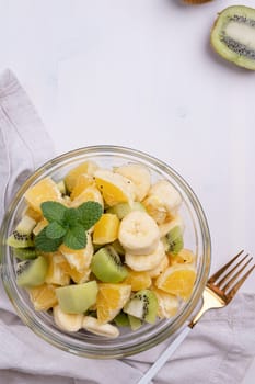 Bowl of healthy fresh fruit salad on white wooden background. Top view.