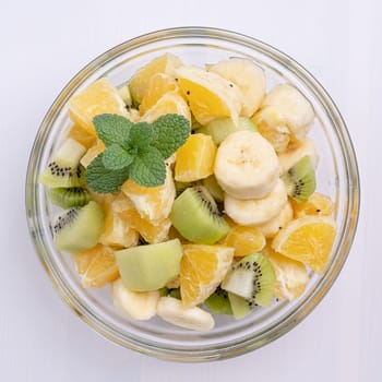 Bowl of healthy fresh fruit salad on white wooden background. Top view.