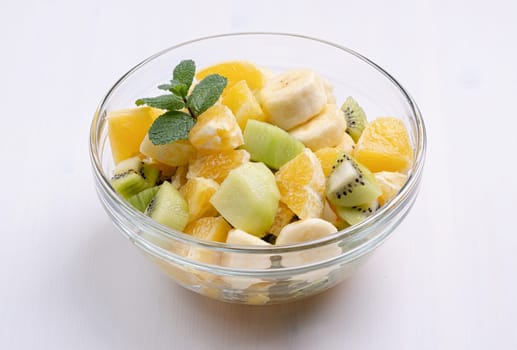 Bowl of healthy fresh fruit salad on white wooden background. Top view.