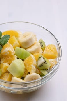 Bowl of healthy fresh fruit salad on white wooden background. Top view.