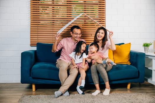 A happy family sitting on a cozy sofa holds a cardboard roof mockup symbolizing safety and protection during their home relocation. Joy and support from parents and their son are evident.