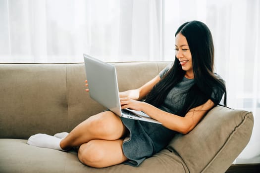Woman on sofa enjoys using laptop for ecommerce watching videos learning. Engaged in studying success and relaxation at home. Modern technology for education and shopping.