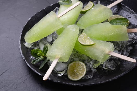 Homemade lime and mint popsicles stacked on a plate with ice on a black background. Copy space.