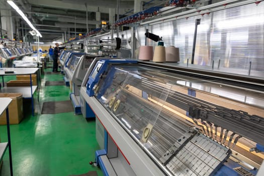 A row of industrial textil flat knitting machines in a knitwear factory. An industrial line of modern automatic knitting machines arranged in two rows.