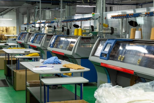 A row of industrial textil flat knitting machines in a knitwear factory. An industrial line of modern automatic knitting machines arranged in two rows.