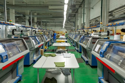 A row of industrial textil flat knitting machines in a knitwear factory. An industrial line of modern automatic knitting machines arranged in two rows.