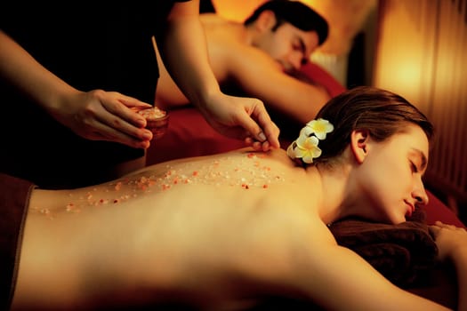 Couple customer having exfoliation treatment in luxury spa salon with warmth candle light ambient. Salt scrub beauty treatment in Health spa body scrub. Quiescent