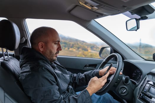 A man is sitting in a car and focused on typing a text message on his smartphone. This image captures urban lifestyle and technology, showcasing modern communication habits.