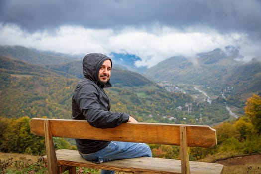 A traveler sits on a wooden bench at an observation point, gazing at the breathtaking mountain scenery, surrounded by nature's beauty and tranquility.