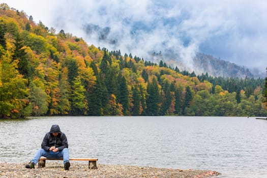 A man admires the picturesque scenery by the lake in the mountains, enjoying the tranquility and beauty of nature.