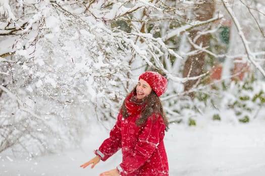 Happy girl in red jumpsuit, knocking down branches with snow and laughing.