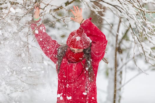 Happy girl in red jumpsuit, knocking down branches with snow and laughing.