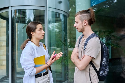 Meeting of two teenage students, guy and girl, outdoors near educational building. Friendship, communication, education, high school college concept