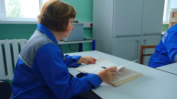 Elderly woman takes notes in laboratory. Clip. Female dispatcher in uniform writes in log. Dispatcher records data on devices in technical log.