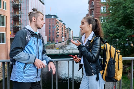 Outdoor meeting of two teenage students, guy and girl, modern city background. Friendship, communication, education, high school, college concept