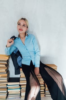 Beautiful fashionable female teacher sitting on stacks of books