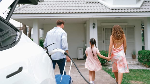 Happy family return from holiday and travel while recharging electric EV car's battery at home charging station. EV car and modern family concept. Synchronos