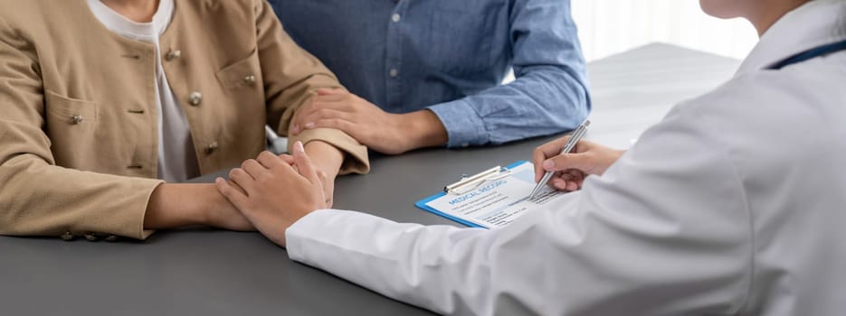 Doctor providing compassionate healthcare consultation while young couple patient holding hand, comfort each other after infertile report. Reproductive and medical fertility consulting. Neoteric