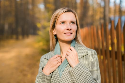 Blonde woman in elegant gray coat walks in the sunny autumn season park. Generation z and gen z youth concept