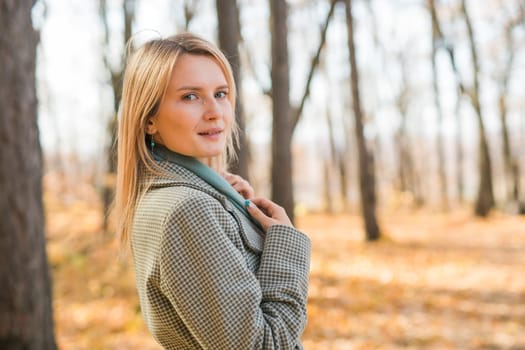 Blonde woman in elegant gray coat walks in the sunny autumn season park. Generation z and gen z youth concept