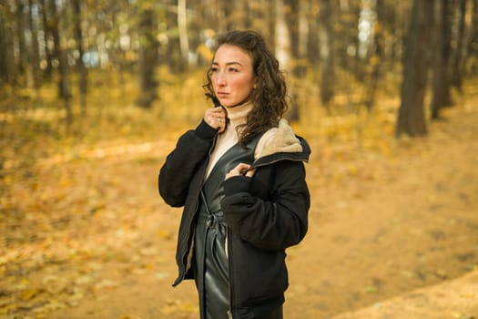 Attractive young woman walking in autumn park, happy mood and fashion style trend and curly long brown hair. Fall season and pretty female portrait. Millennial generation