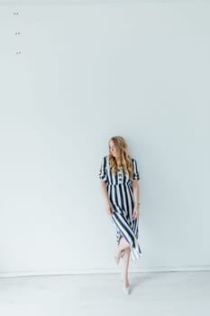 Beautiful blonde woman in summer striped dress against white wall