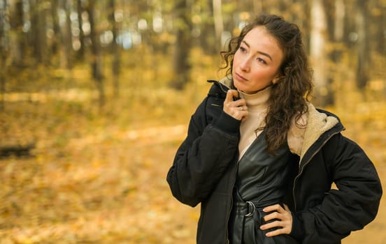 Attractive young woman walking in autumn park, happy mood and fashion style trend and curly long brown hair. Fall season and pretty female portrait. Millennial generation