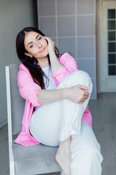 Beautiful fashionable brunette woman sitting on a chair in pink jacket and white pants