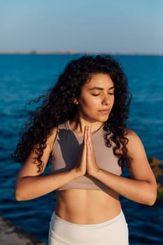 Woman doing yoga asana gymnastics breathing practice on the beach by the sea