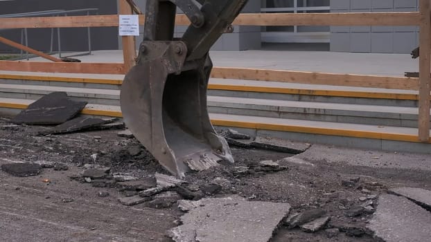 Close-up of excavator breaking asphalt. Clip. Excavator removes layer of old asphalt on summer day. Excavator changes road surface on roads.