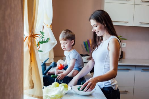 kitchen little son helps mom wash fruits and vegetables in the sink