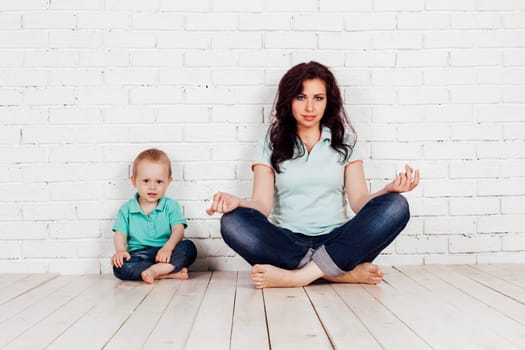 mom and young boy son sit on the floor white brick wall