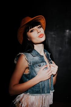 beautiful sexy girl in cowboy hat and denim waistcoat on a black background