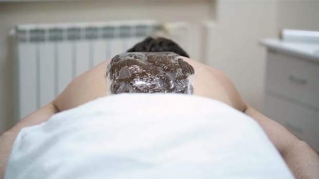 Close-up of man's back during chocolate body wrap treatment. Rest in spa