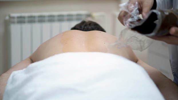Close-up of man's back during chocolate body wrap treatment. Rest in spa