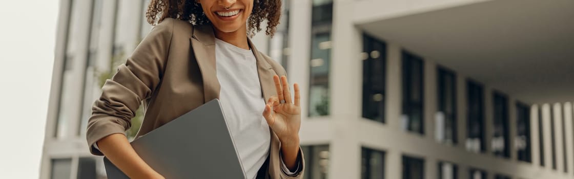 Stylish female manager standing with laptop on office building background during break time