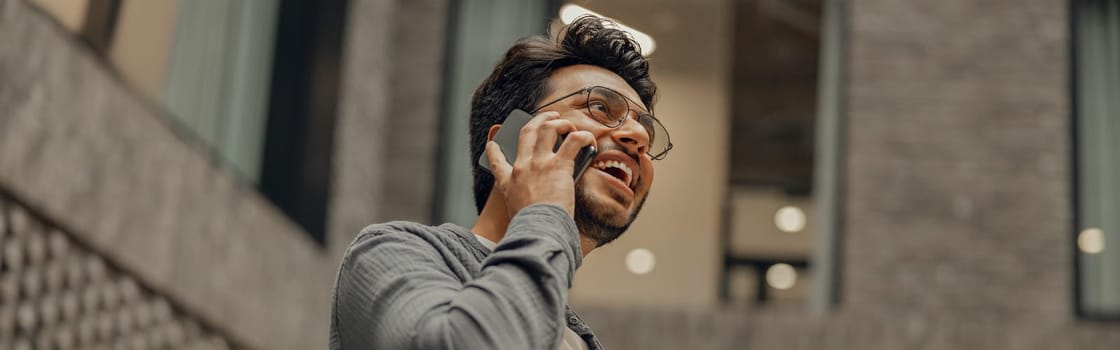 Bearded male freelancer in eyeglasses is talking phone standing in modern coworking space