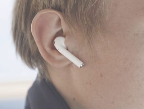 Man wearing wireless white headphones. Stock. Close-up of man wearing small Bluetooth headphones. Modern comfortable headphones with excellent sound.